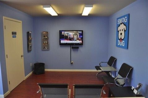 The Smog Dog waiting room: blue walls, a wall-mounted TV, magazine racks, black chairs and a framed Smog Dog poster